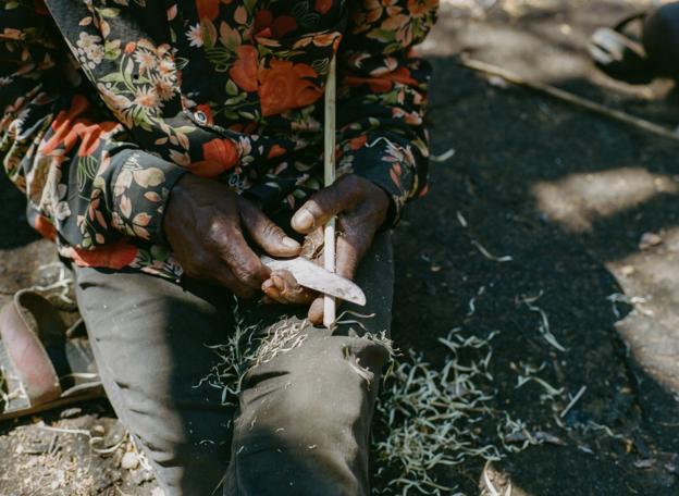 A Hadza tribesperson whittles a wooden arrow shaft