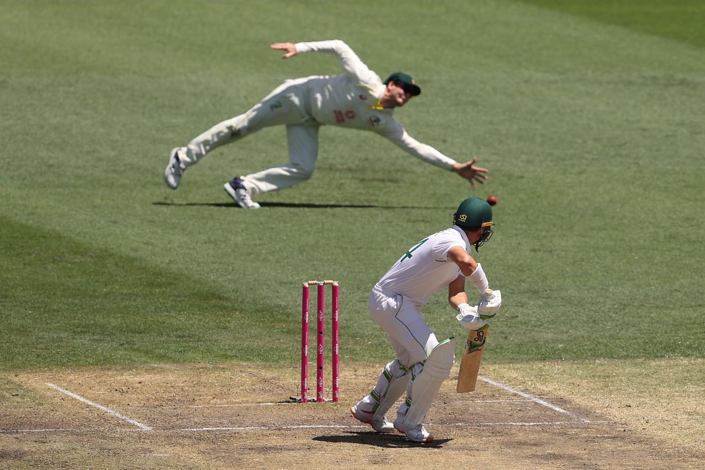 Australia fielder Steve Smith dives to try to catch a cricket ball with one hand as South Africa batter Dean Elgar looks back at it.