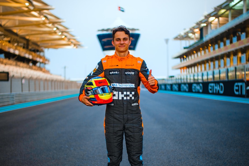 A man holding a helmet stands on a race track.