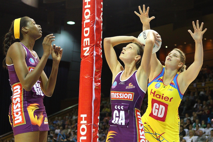 Medhurst holds the ball over her head as she looks up to the netball post