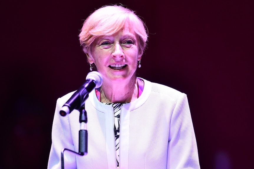 Liz Nicholl stands at a lectern and smiles as she delivers a speech
