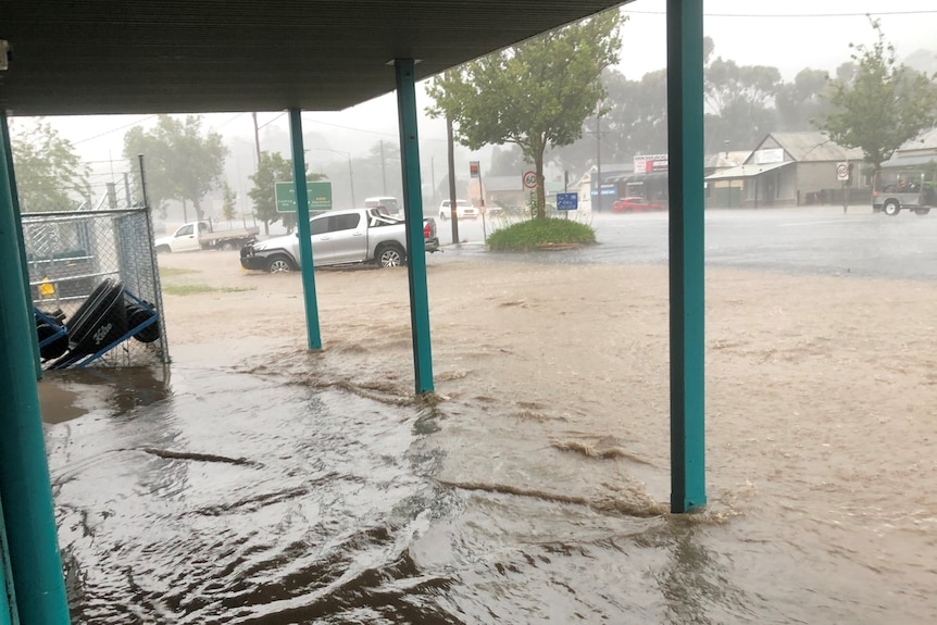 A flooded wide verandah with green posts, streets are also flooded with four-wheel drive marooned.
