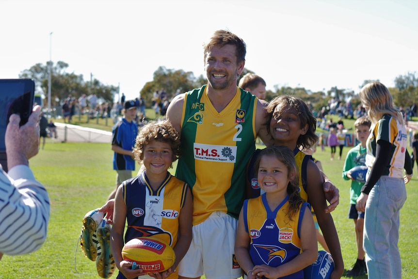 Man in green and gold football uniform with three children in Eagles jersey's smiles for a photo 