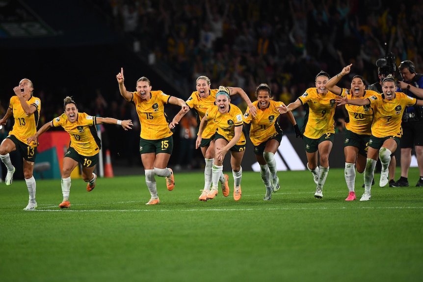 A group pf athletes in yellow shirts celebrate wildly.