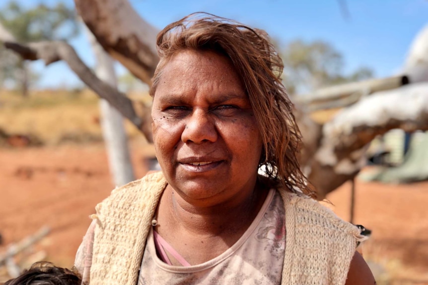 An Aboriginal woman stands smiling at the camera with the Kimberley desert in the background.