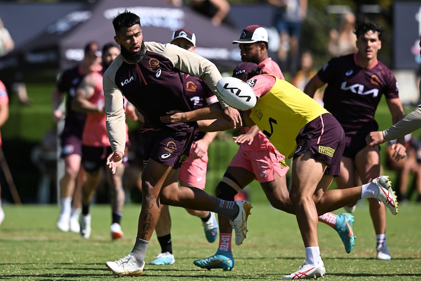 A Brisbane Broncos player flexes his right hand after offloading the ball to his left in a training drill.