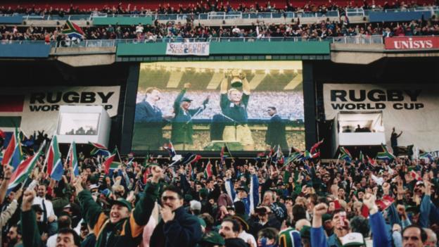 Fans inside Ellis Park cheer as South Africa captain Francois Pienaar lifts the Rugby World Cup in 1995