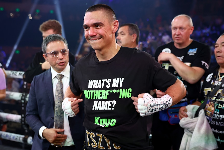 Tim Tszyu points to a slogan on his black tshirt that reads 'What's my mottherf***ing name?' with Kayo branding