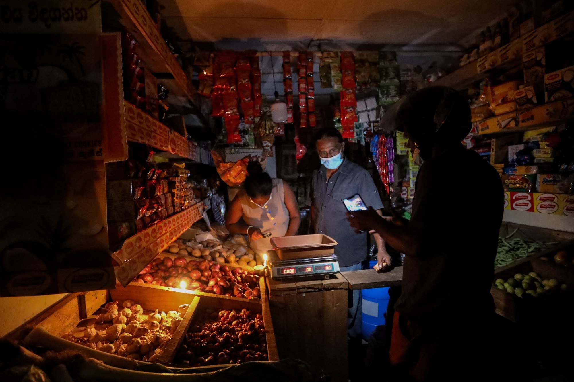 A grocery vendor illuminates his shop with candlelight amid power cuts in Colombo, Sri Lanka, in March 2022. Electricity tariffs have crippled many small businesses. Photo: EPA-EFE