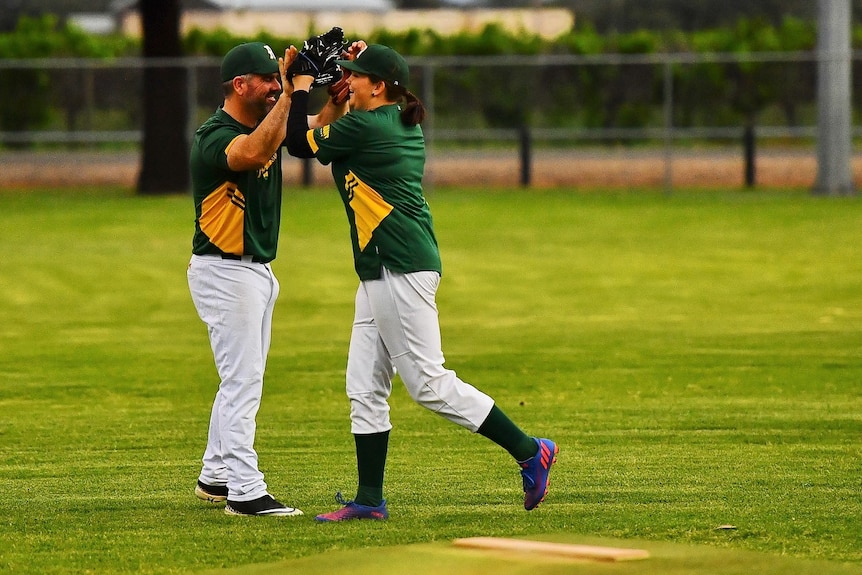 A smiling man high-fives a smiling young woman on a baseball diamond.
