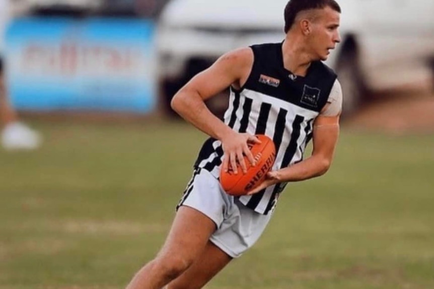 A man in black and white football gear running on a field, holding a ball.