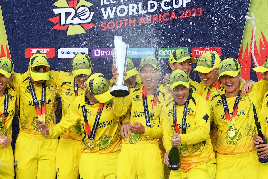 Australian players smile and laugh as they spray champagne and celebrate with a trophy on a podium