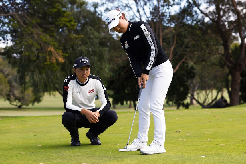 Min Woo Lee crouches down and watches Minjee Lee hit a putt in a staged photo