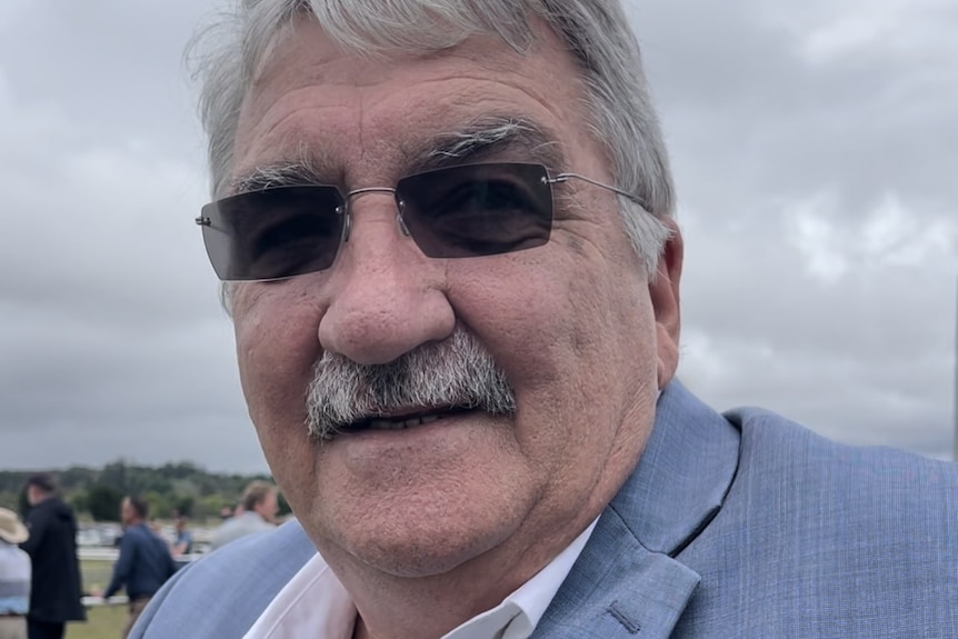 Grey haired man in blue suit wearing dark glasses