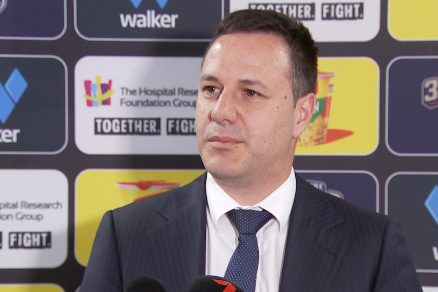 A man standing in a suit with a sports background