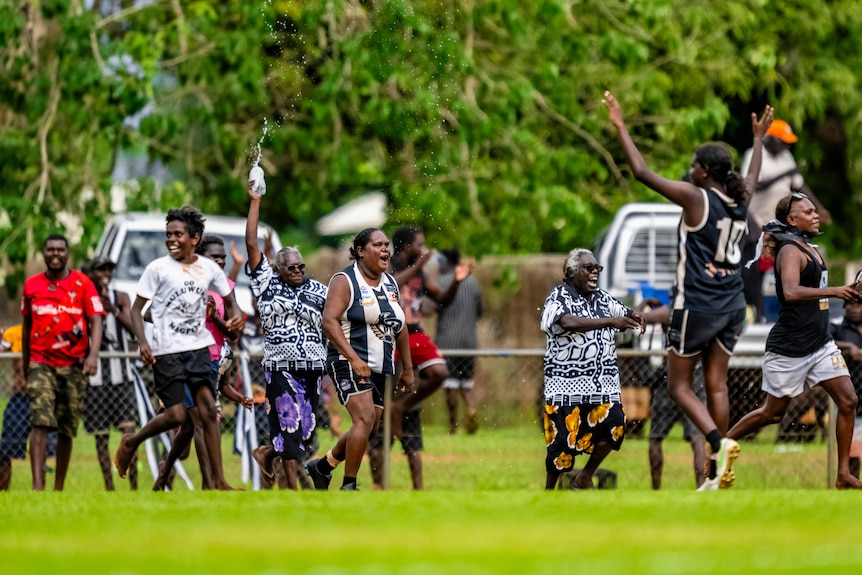 Players and supporters celebrate on the footy oval.