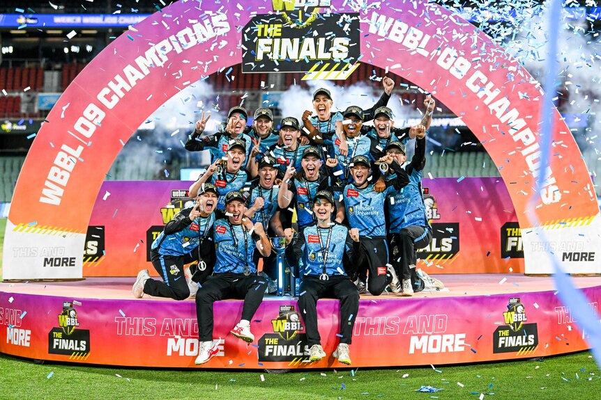 Strikers players huddle together on the podium with the trophy as confetti flies overhead