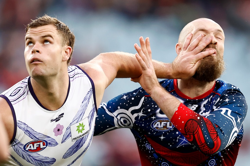 A Fremantle AFL player puts his left hand in the face of a Melbourne opponent.