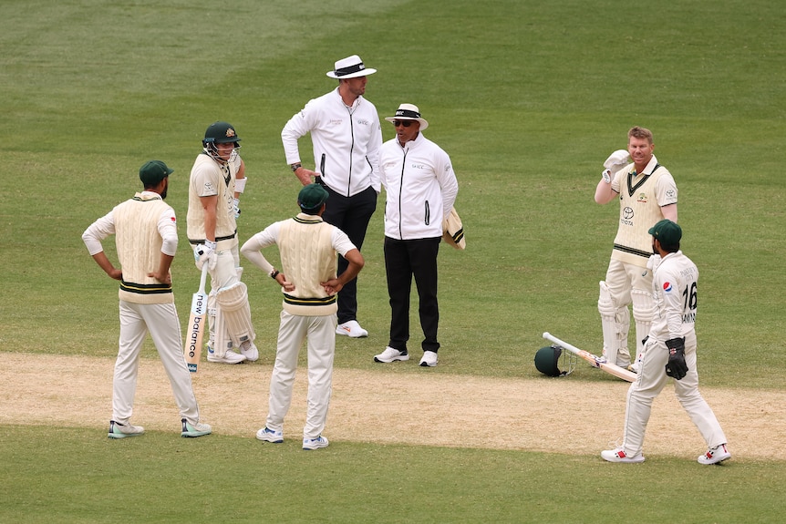 Pakistan and Australia players speak to umpires during a delay on the MCG pitch.