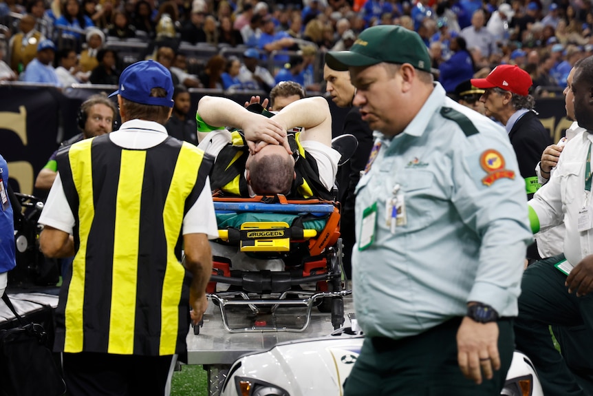 A staff member is wheeled off the pitch holding his face