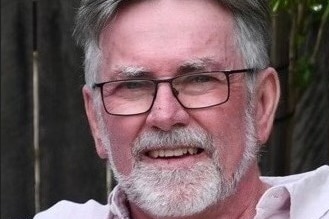 man with grey hair and glasses smiles at camera wearing a pink shirt 