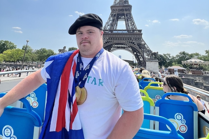 boy stands in front of Eiffel tower wearing Australian flagged draped over shoulder 