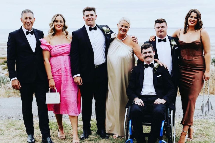 a family stand together wearing formal dresses and suits
