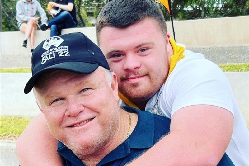 boy stands hugging a man wearing a cap 
