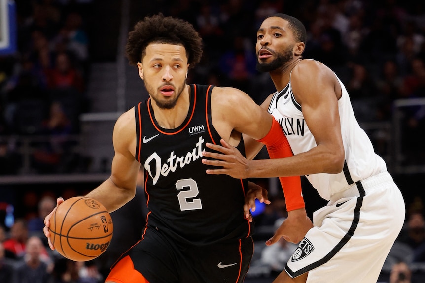 A medium shot of a male basketball player dribbling the ball past an opposing player during an NBA game.