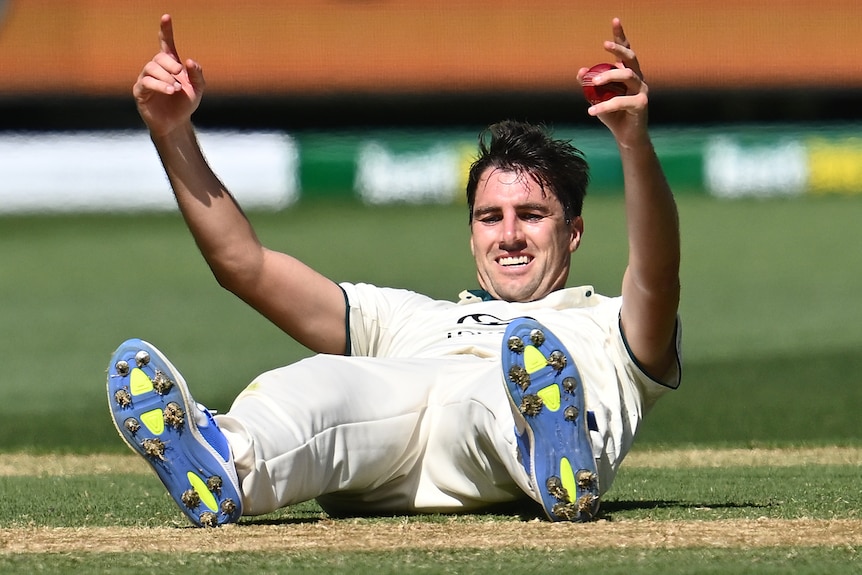 Pat Cummins sits on the floor with his hands up
