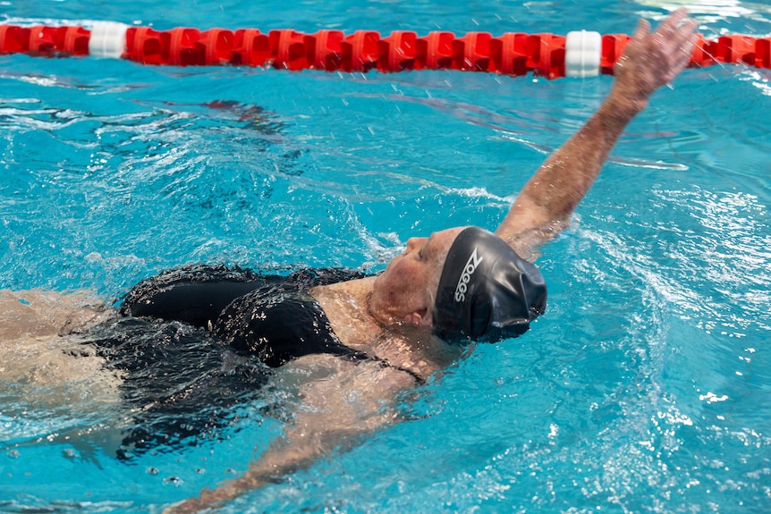 An elderly woman swimming laps in a pool