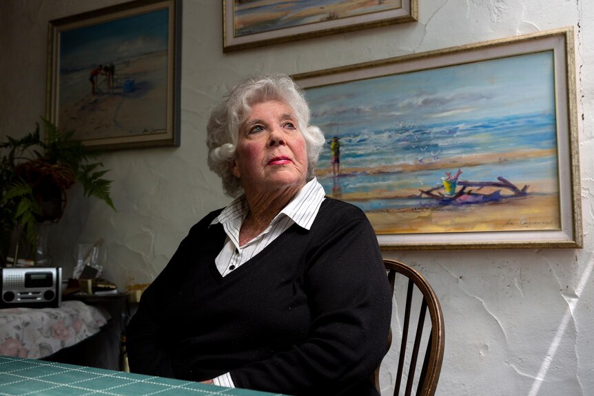 An elderly woman ponders out a kitchen window