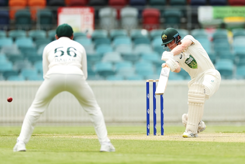 A Prime Minister's XI cricketer hits an off-drive past a Pakistan fielder towards the boundary. 