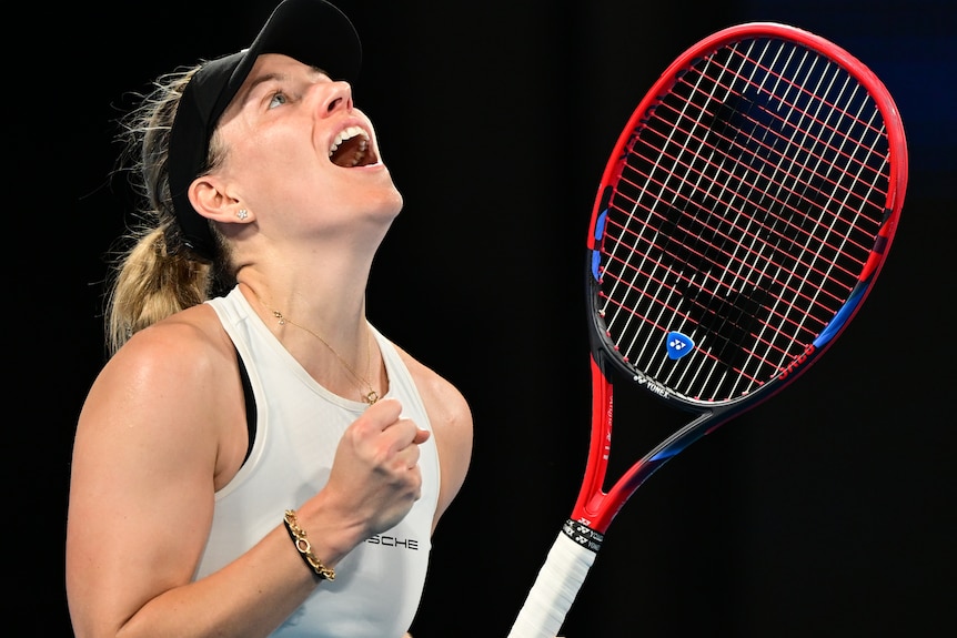 A woman holds a tennis racquet in one hand and her other hand has her fist clenched.