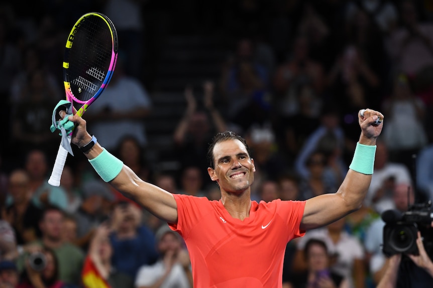 Rafael Nadal holds up his tennis raquet and arms and smiles.