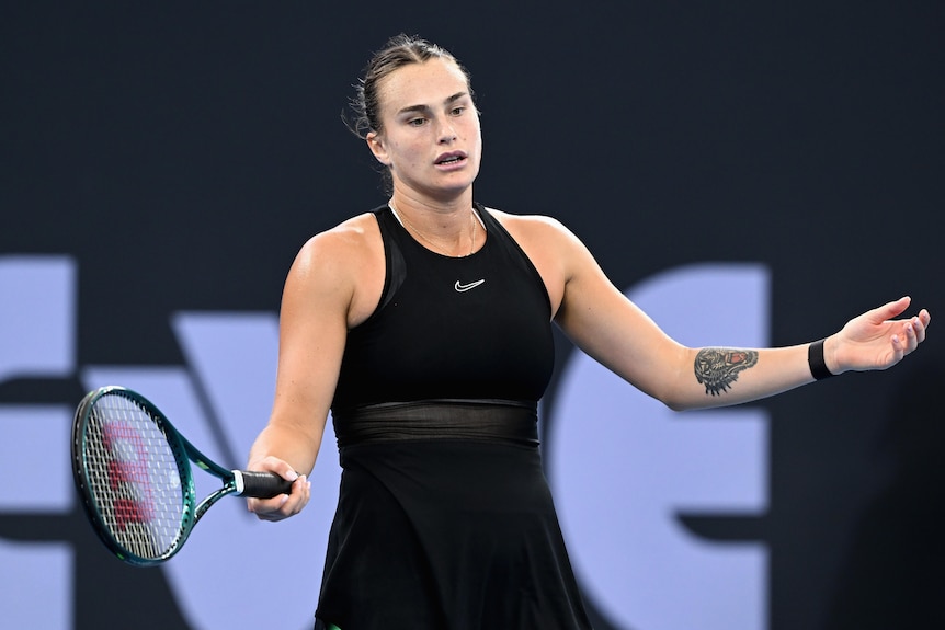 A tall tennis player stares down at the court in frustration as she gestures with her racquet and arms.