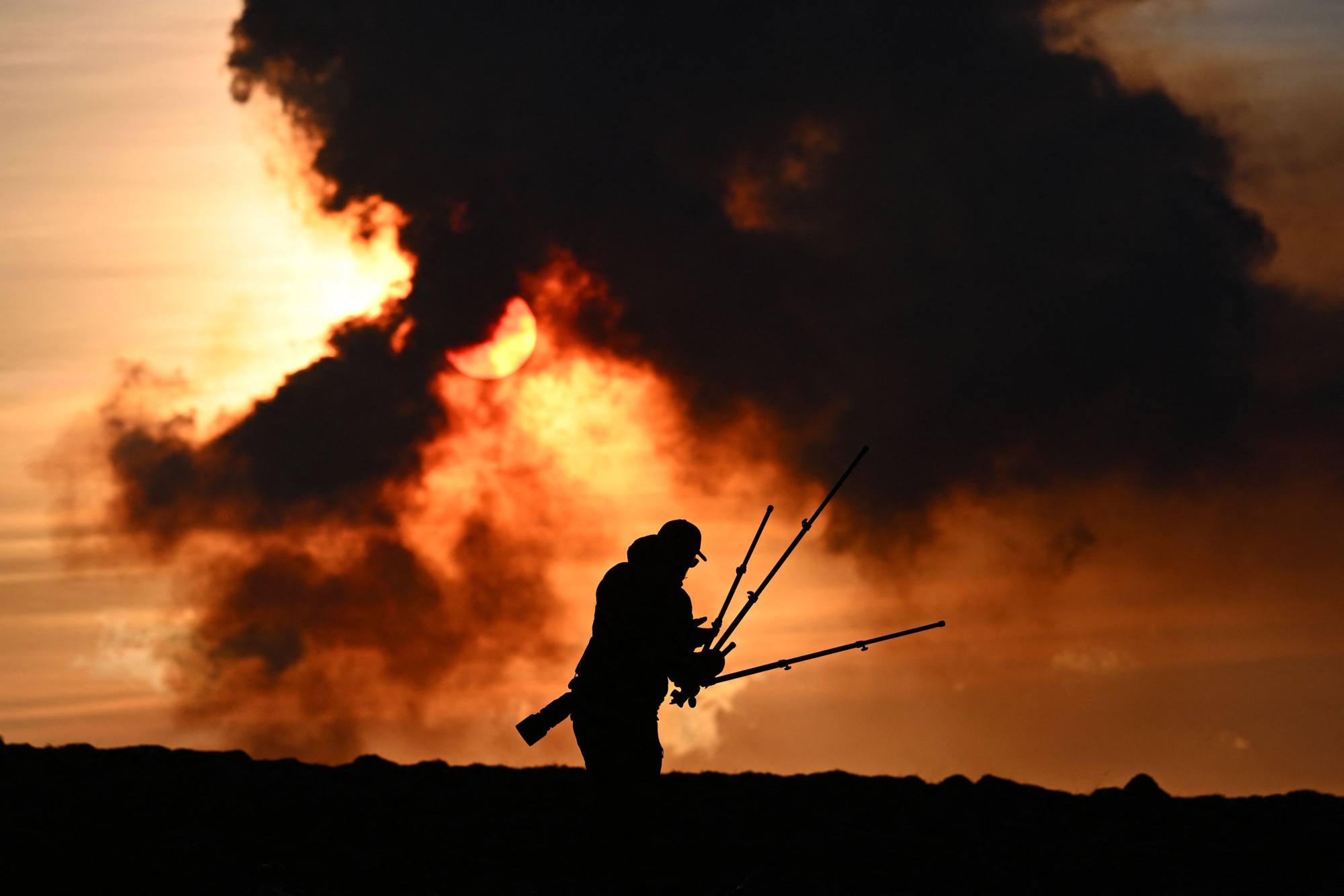 A man adjusts his photographic equipment near Keflavik, Iceland, as plumes of smoke rise during a volcanic eruption near Grindavík, on Sunday. Photo: AFP