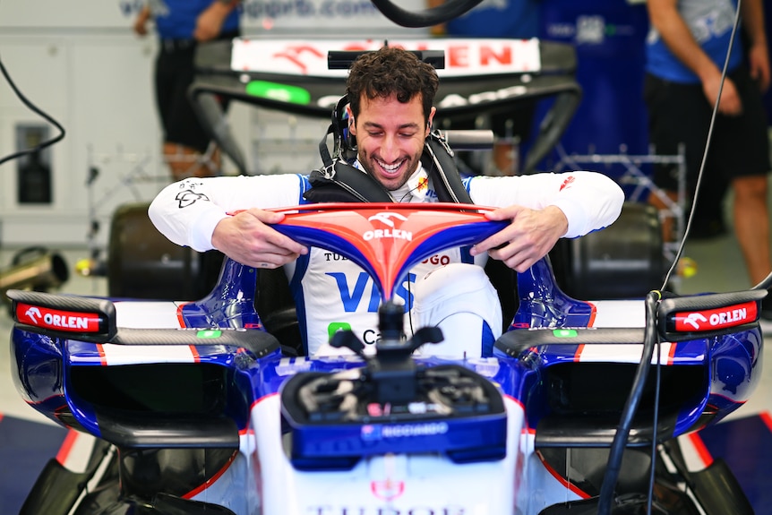 Male F1 driver Daniel Ricciardo lowers himself into his car, ready to race.