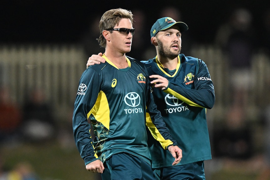 An Australian bowler smiles as a teammate puts his arm around his shoulder in celebration after a wicket. 