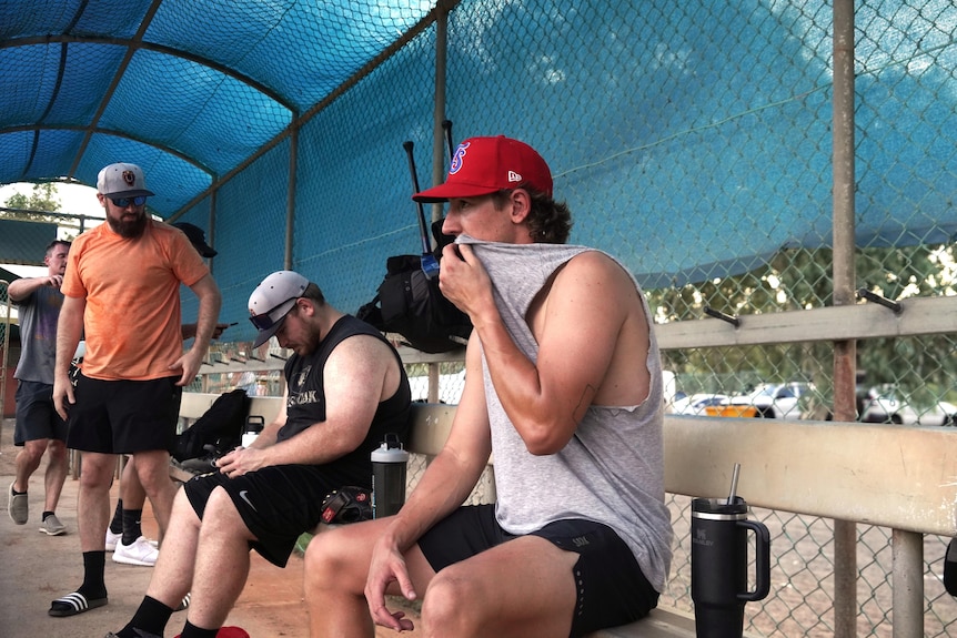 Men stand and sit on a bench at baseball training.