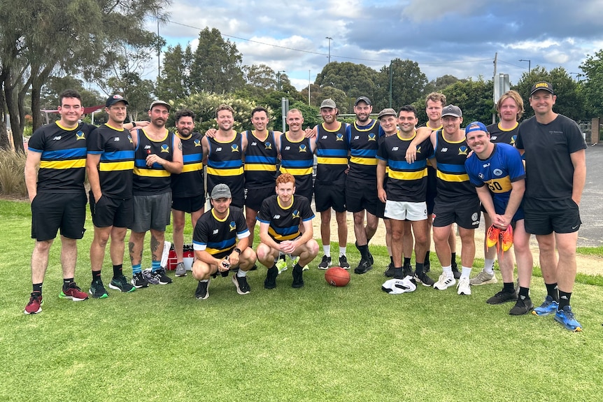 Eighteen men in football outfits smile at the camera