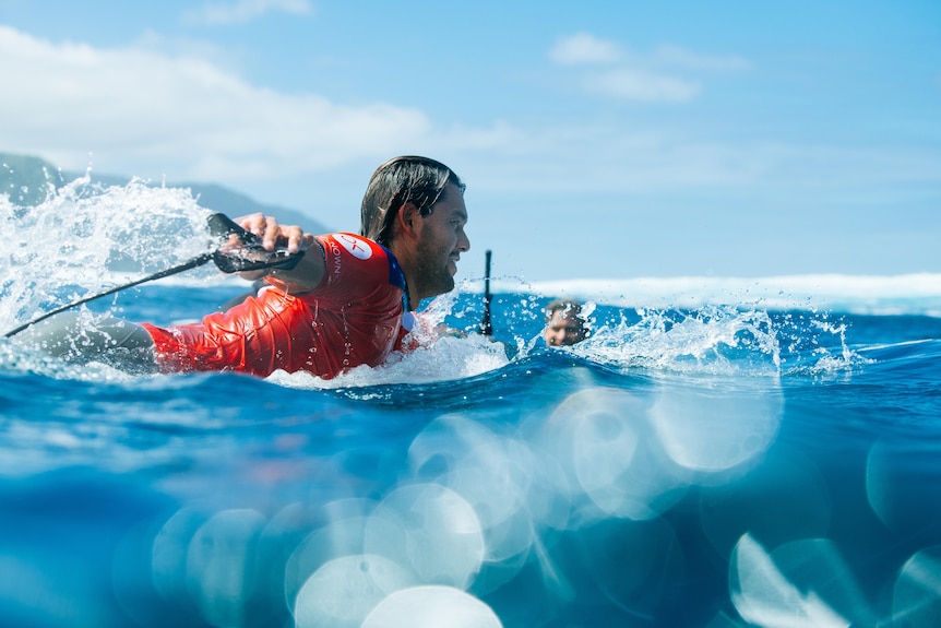 A photo looking through the water at a surfer paddling out from shore before a heat of a competition.