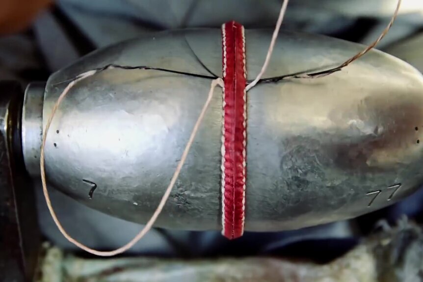 Metal concave shape wrapped around cricket ball exposing seam being sewn