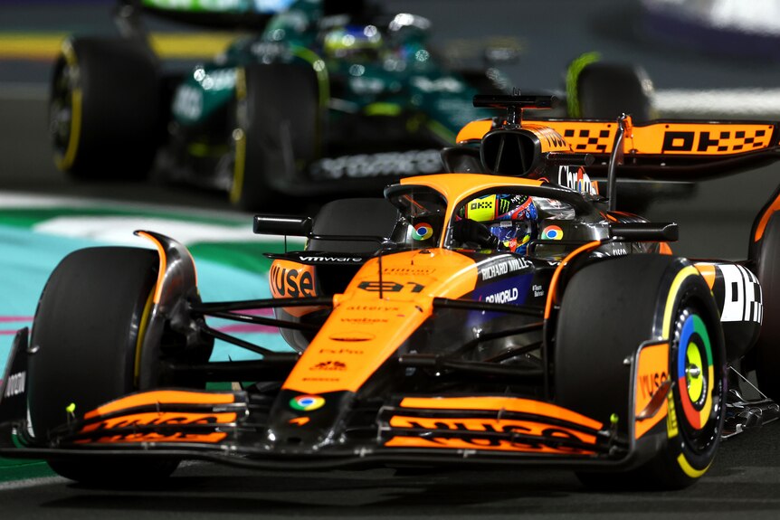 Oscar Piastri in his orange McLaren, driving around a corner during a night race.