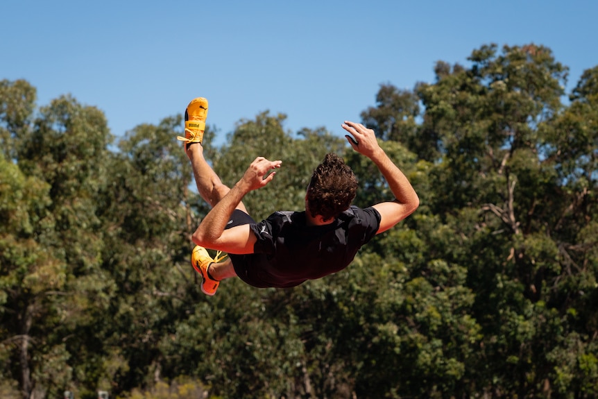 A man in activewear trains at an athletics stadium on a sunny day.
