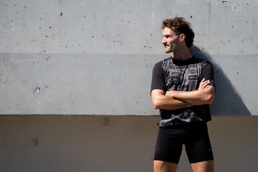 A man in activewear trains at an athletics stadium on a sunny day.