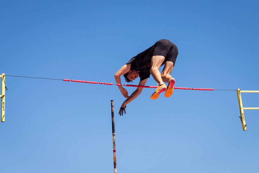 A man in activewear trains at an athletics stadium on a sunny day.