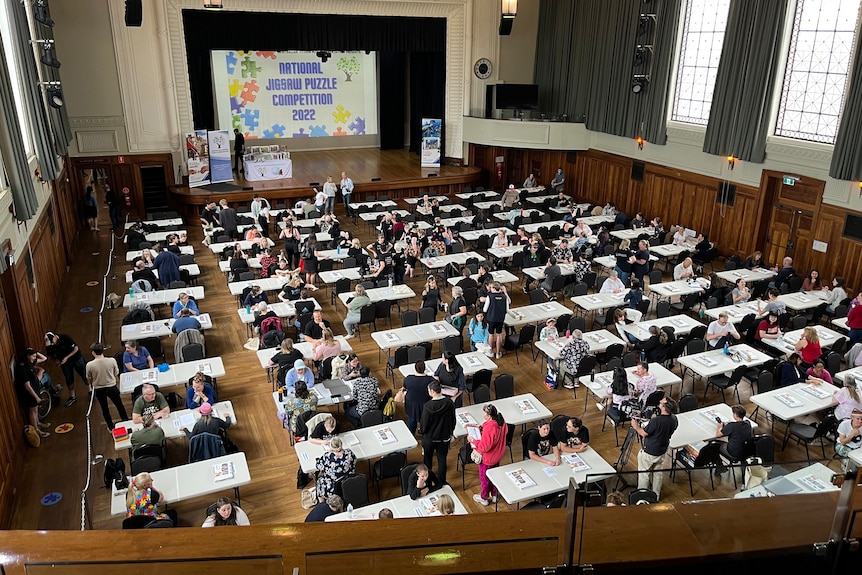 Hall of people sitting at tables, waiting to compete in a puzzle competition.