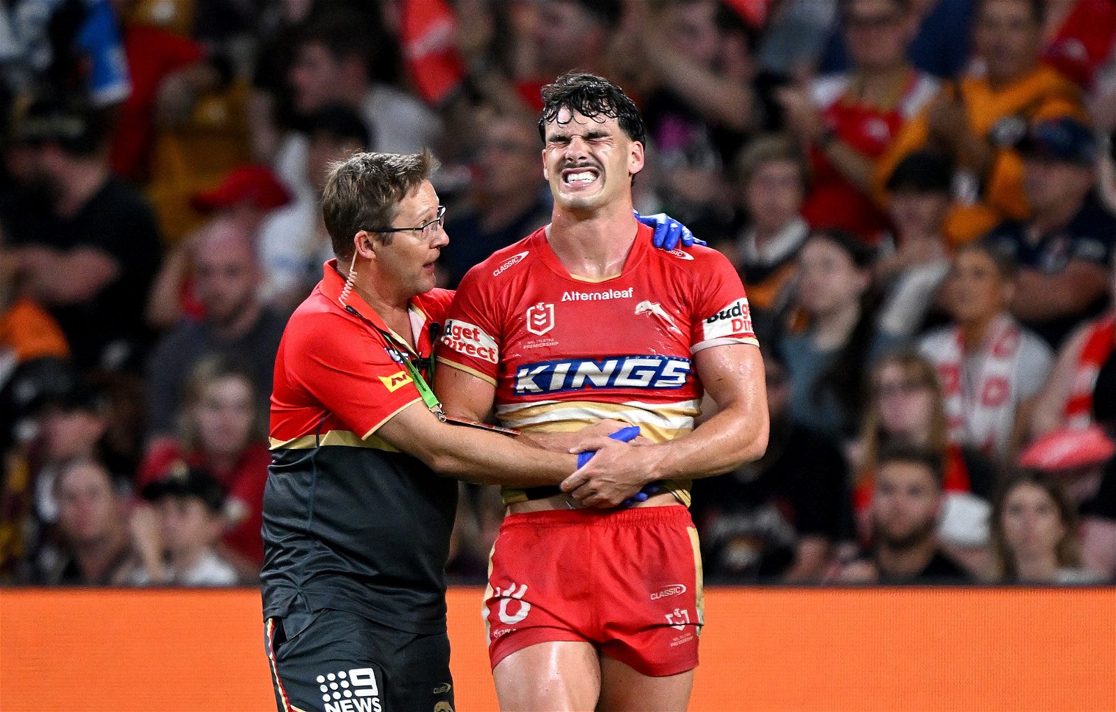 Herbie Farnworth grimaces while in the care of a trainer during an NRL game for the Dolphins.