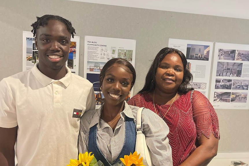 A young woman holding flwoers standing next to her mum and brother.